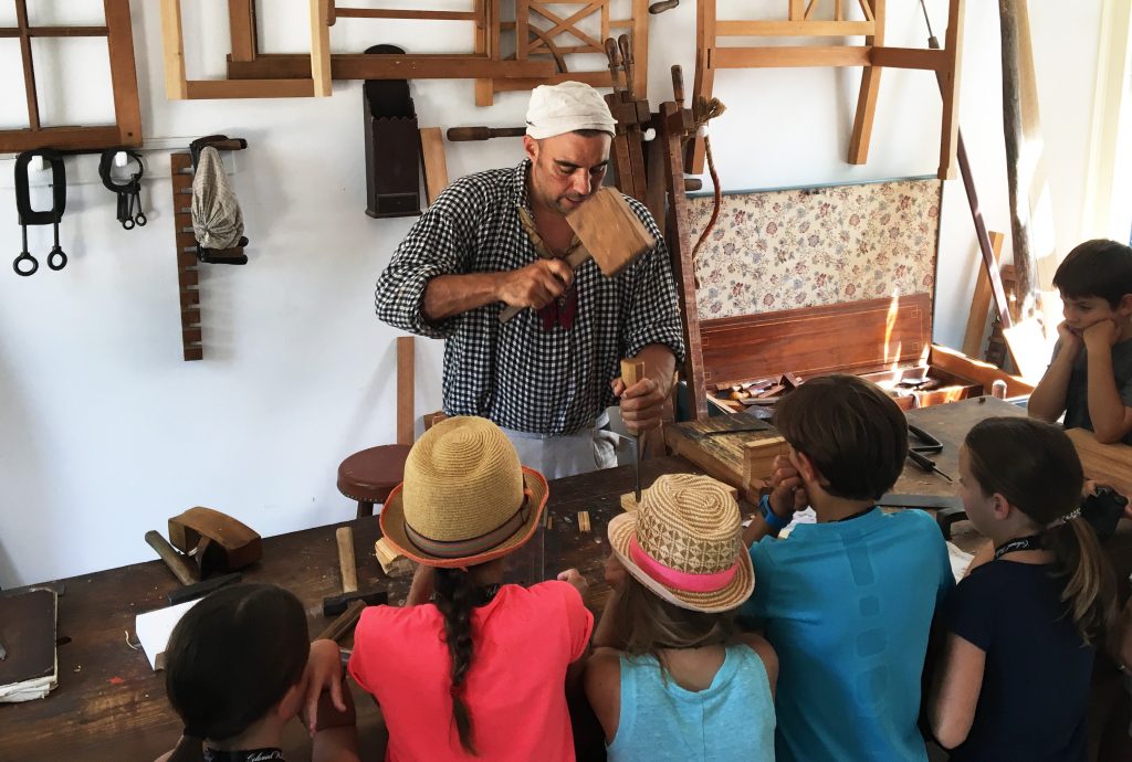 A living history docent shows how he creates wood materials and frames by carefully working the wood into different configurations. This is one of the many Colonial buildings that you must purchase a Colonial Williamsburg pass to be able to see. (Kevin Kaiser | Travel Beat Magazine)